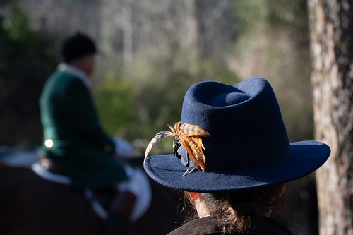 Blue hat with feather in foreground, hunt rider in the back.