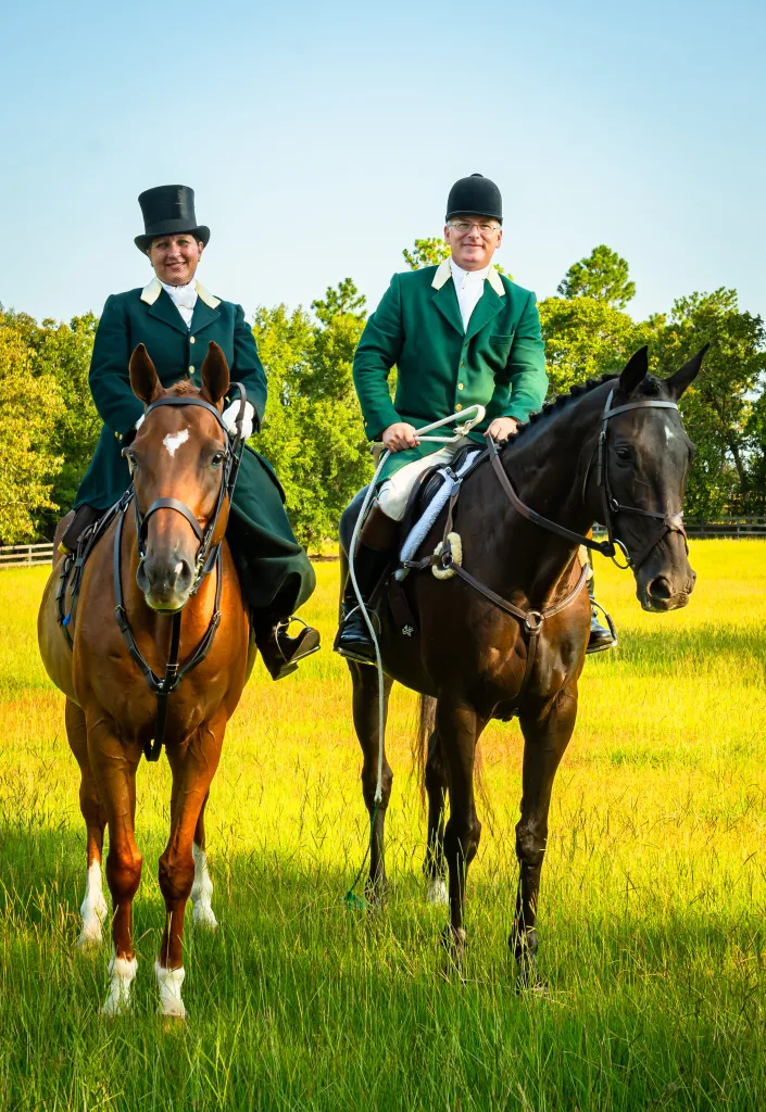 Two mounted hunt riders in formal attire, one side saddle.