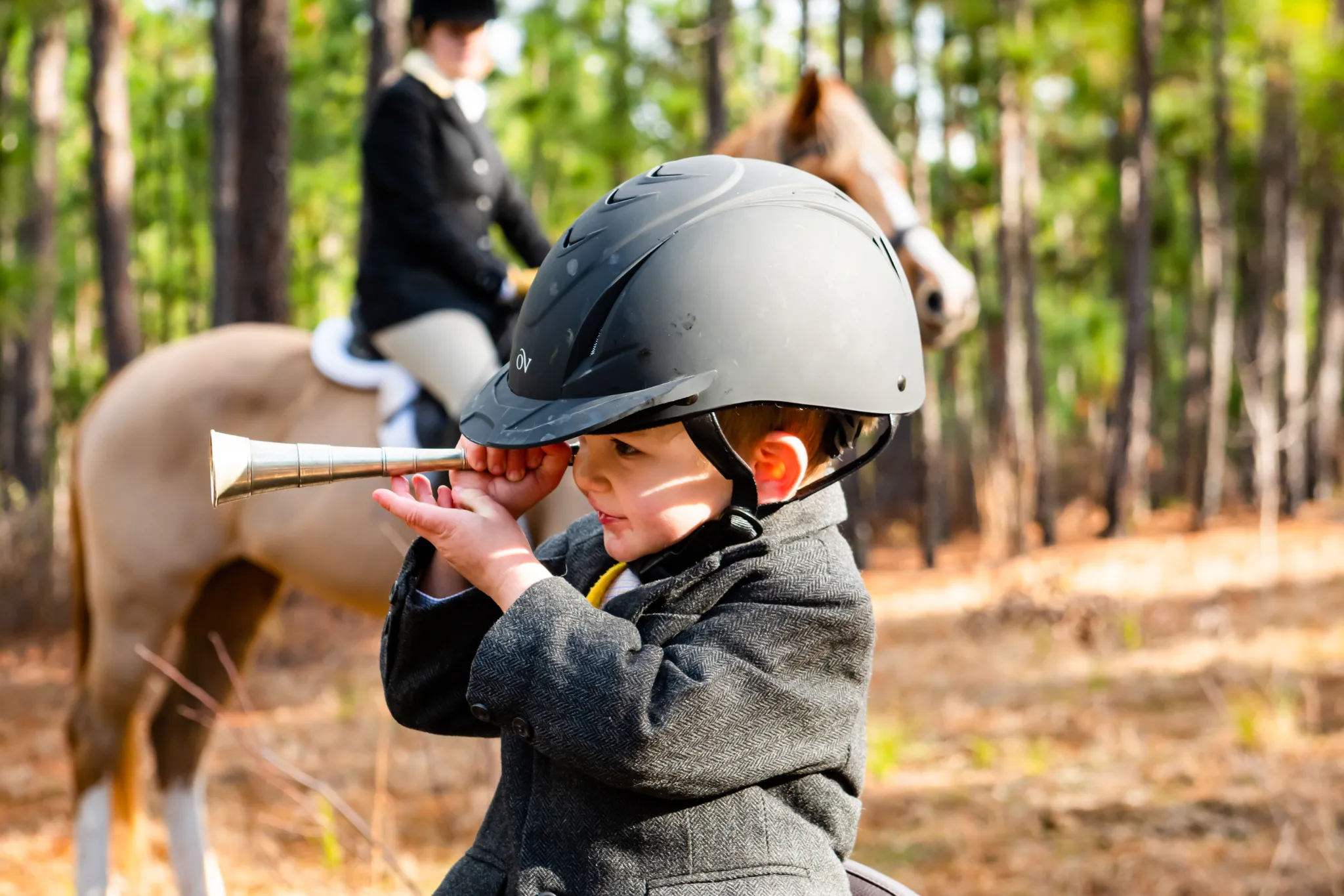 Small child with helmet and tweed coat looking through end of horn.